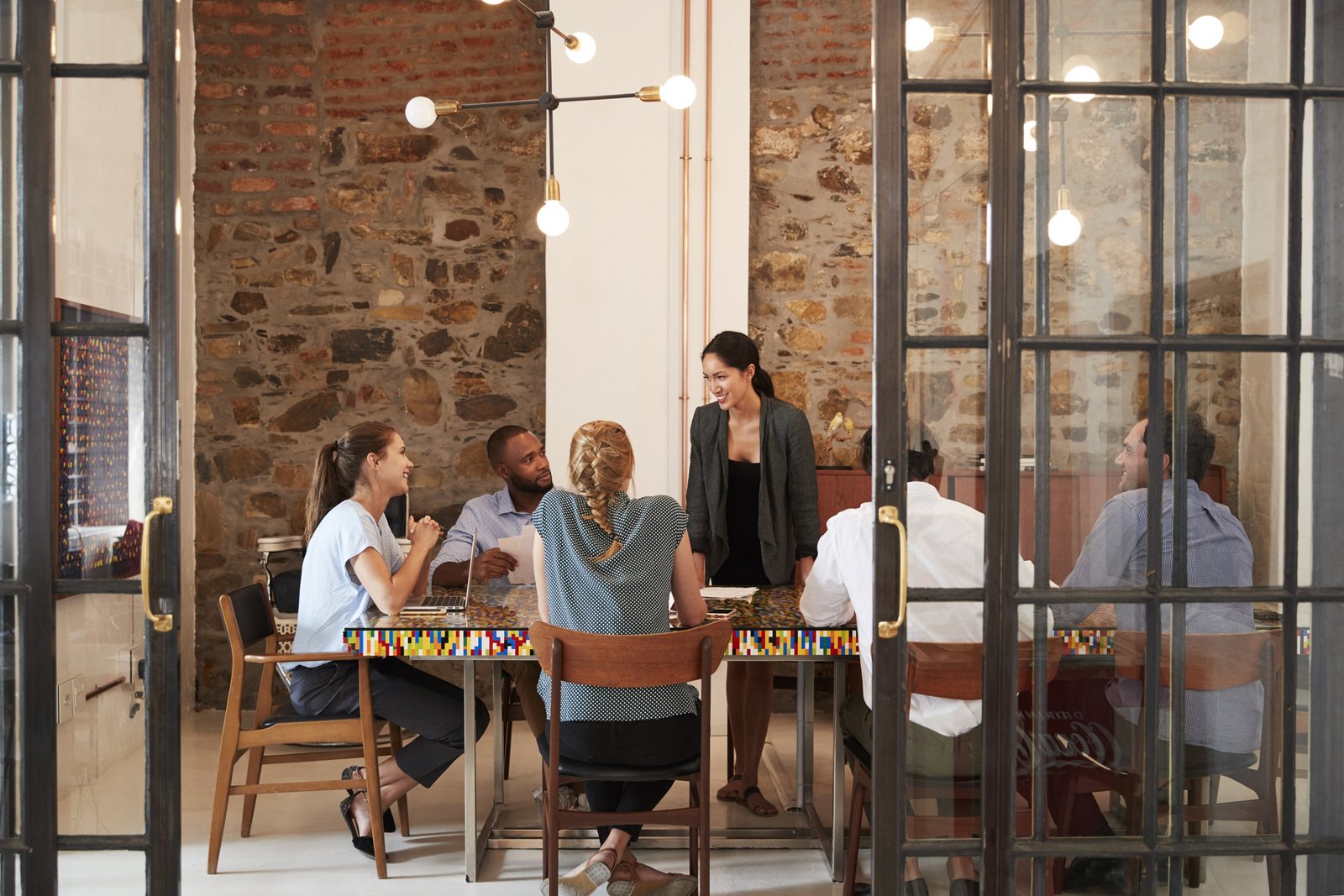 Team meeting around a table in a glass-walled office.